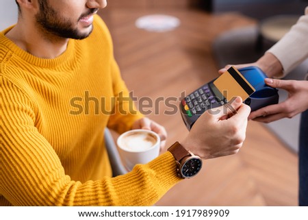 partial view of arabian man paying through payment terminal in hands of waitress Royalty-Free Stock Photo #1917989909