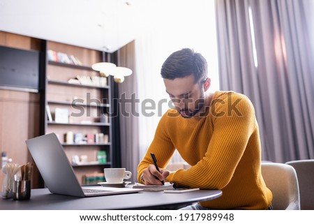 focused freelancer writing in notebook near laptop in restaurant