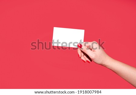 Female hands with beautiful manicure hold a discount card, business card, mockup of a blank white sheet of paper on a red background with copy space. Template for design. layout. copy space for text