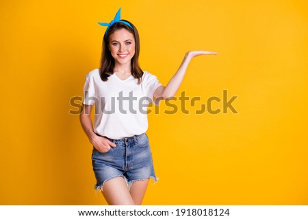 Photo of young brown haired woman show empty space display ad hand wear white t-shirt blue pin-up isolated on bright color background