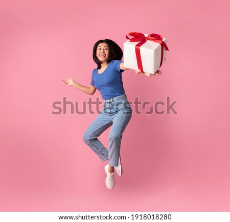 Full length vertical photo of jumping high excited asian lady holding and showing present box close to camera, giving gift isolated over pastel pink studio background. Greeting And Celebration Royalty-Free Stock Photo #1918018280