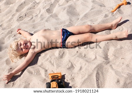 Little boy lying on the sand and playing on the beach of Mediterranean sea. Summertime, vacation, travel concept.