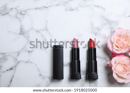 Different lipsticks and beautiful flowers on white marble table, flat lay. Space for text