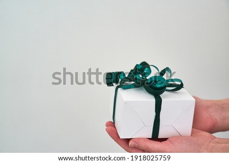 Female hands are holding a small gift wrapped in a green ribbon close-up on a white background. Copy space