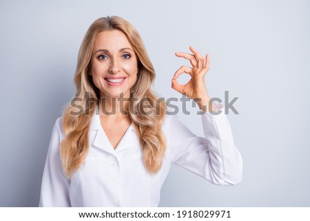 Photo of mature attractive charming smiling positive woman doctor showing okay sign isolated on grey color background