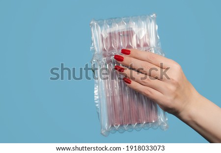 Closeup view color stock photography of female hand holding her online order wrapped in protective plastic air pack for shipping safely fragile goods