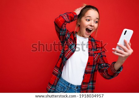 Photo of attractive crazy amazed surprised young woman wearing casual stylish clothes standing isolated over background with copy space holding and using mobile phone looking at device screen