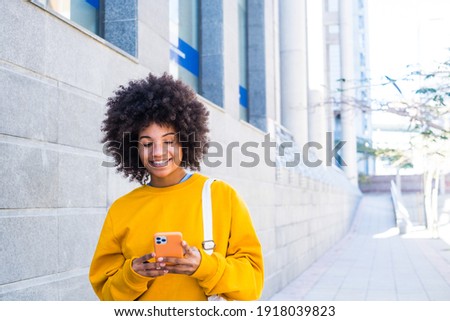 beautiful African or American young woman walking in the street of the city looking at her phone smiling and having fun enjoying Royalty-Free Stock Photo #1918039823