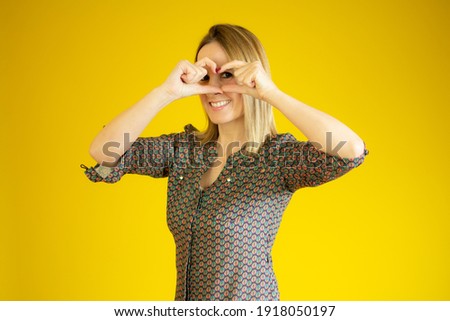 Pretty blonde girl in a casual shirt making heart figure with her hands