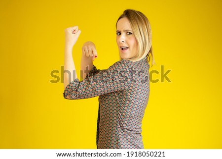 Successful woman raising hand in success gesture over yellow background