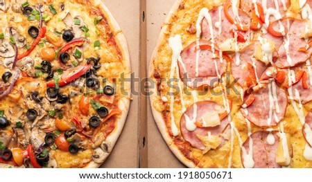 two pizzas with mushrooms and pepperoni salami, ham, olives, cheese, pepper, cherry tomatoes in paper delivery boxes, top view, close up