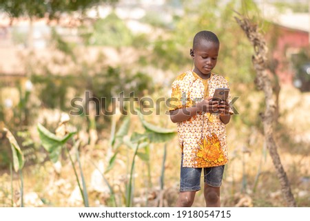 african child standing outdoor and using a mobile phone Royalty-Free Stock Photo #1918054715