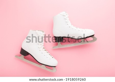 White female figure skates on light pink table background. Sport accessories for activities. Closeup. Pastel color. 