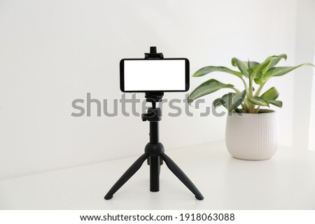 Smartphone with blank screen fixed to tripod on white table indoors. Mockup for design Royalty-Free Stock Photo #1918063088