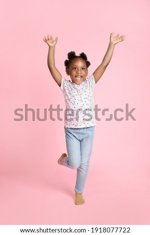 Smiling happy little african american kid girl 6-7 years old wearing casual clothes, standing with hands raised up, looking away and isolated on pink background. Childhood lifestyle concept Royalty-Free Stock Photo #1918077722