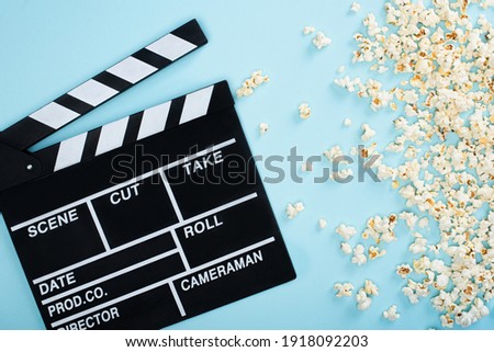 top view of clapperboard near popcorn scattered on blue, cinema concept