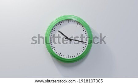 Glossy green clock on a white wall at seventeen past ten. Time is 10:17 or 22:17 Royalty-Free Stock Photo #1918107005