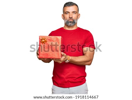Middle age handsome man holding gift thinking attitude and sober expression looking self confident 
