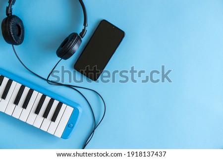 Small light blue piano, headphones and smartphone on light blue background with copy space.