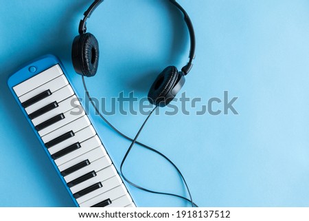 Small light blue piano and headphones on light blue background with copy space.