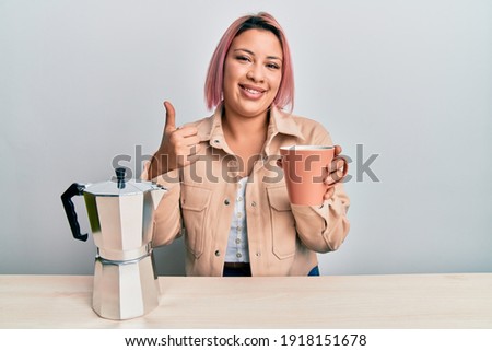 Hispanic woman with pink hair drinking a cup of italian coffee smiling happy and positive, thumb up doing excellent and approval sign 