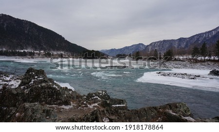 The Katun River seethes among the mountains and forests on a cloudy winter Altai day. Image with selective focus, noise effects and toning.
