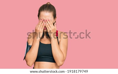 Beautiful blonde woman wearing gym clothes and using headphones rubbing eyes for fatigue and headache, sleepy and tired expression. vision problem 