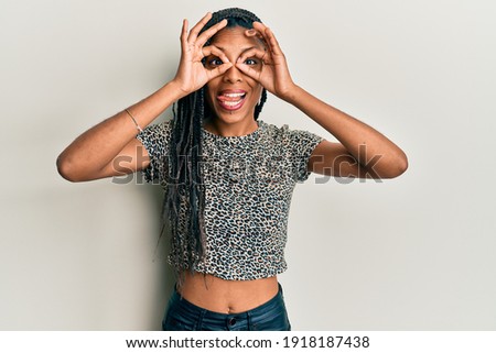 African american woman wearing casual clothes doing ok gesture like binoculars sticking tongue out, eyes looking through fingers. crazy expression. 
