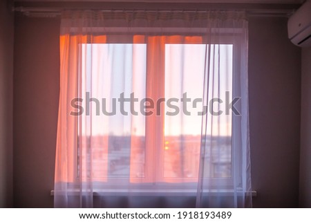 The rays of the morning sun fall through the white tulle on the window in the apartment. Sunrise, new day, atmospheric mood. Royalty-Free Stock Photo #1918193489