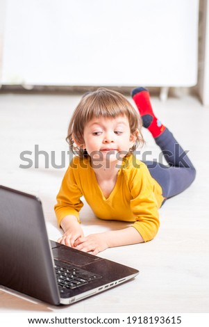 child looking at a laptop while lying on a light floor at home