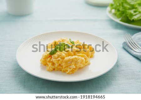 Scrambled eggs, omelette. Breakfast with pan-fried eggs. Texture of omelet on white plate on green mint linen textile tablecloth. Keto ketogenic diet. Soft light Royalty-Free Stock Photo #1918194665