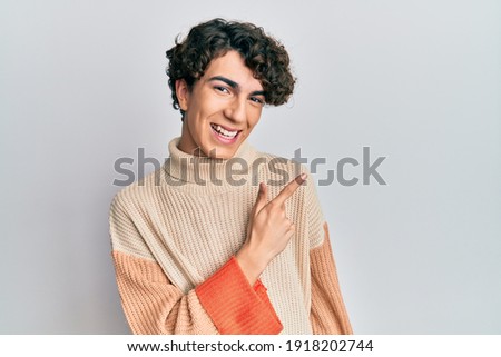 Hispanic young man wearing casual winter sweater cheerful with a smile of face pointing with hand and finger up to the side with happy and natural expression on face 
