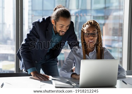 Smiling multiethnic businesspeople gather at desk in office look at computer screen cooperate together. Happy multiracial diverse colleagues work on laptop, brainstorm over company business project. Royalty-Free Stock Photo #1918212245