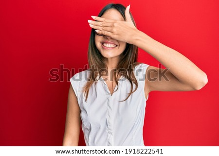 Young brunette woman wearing casual clothes and glasses smiling and laughing with hand on face covering eyes for surprise. blind concept. 