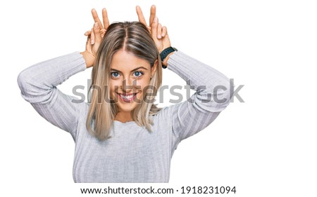 Beautiful blonde woman wearing casual clothes posing funny and crazy with fingers on head as bunny ears, smiling cheerful 