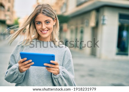 Young blonde girl smiling happy using touchpad at the city.