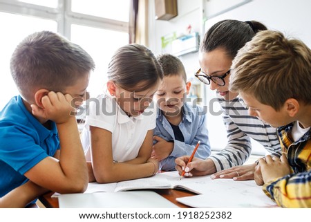 Female teacher helps school kids to finish they lesson.They sitting all together at one desk.	
 Royalty-Free Stock Photo #1918252382