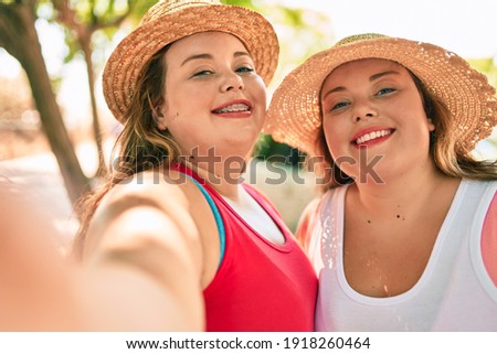 Two plus size overweight sisters twins women smiling taking a selfie picture with the phone outdoors