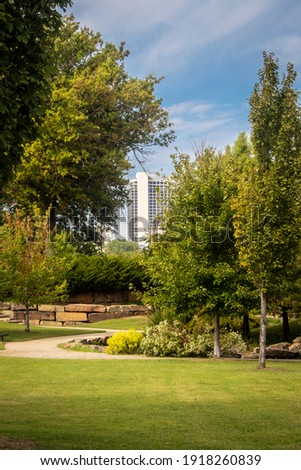 View of tall downtown buildings from curved walks of leafy park on pretty sunny day.
