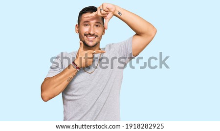 Handsome man with tattoos wearing 90s style smiling making frame with hands and fingers with happy face. creativity and photography concept. 
