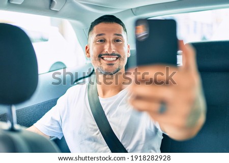 Young hispanic man smiling happy making selfie by the smartphone sitting on the car.