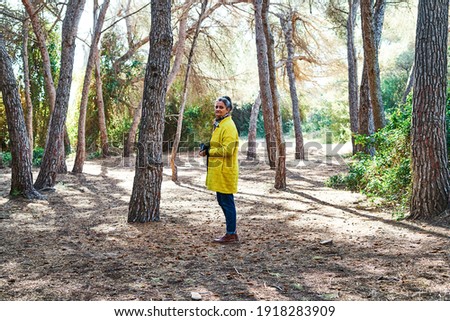 Middle-aged gray-haired brunette woman looks to take pictures with analog reflex camera in the forest