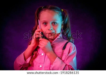 The little girl with surprised face is talking on the phone. Studio photosession - turquoise, magenta and purple neon filters . Royalty-Free Stock Photo #1918286135