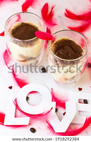 Dessert tiramisu on a white background among red feathers and inscription love