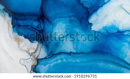 Blue alcohol stains of paint with the addition of gold powder. Subtle waves of paint, abstract blue waves of the ocean, lines of marble. Liquid paints, gradient stains, painting.