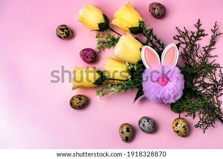 toy fluffy easter bunny sitting next to carrots, easter eggs and artificial flowers