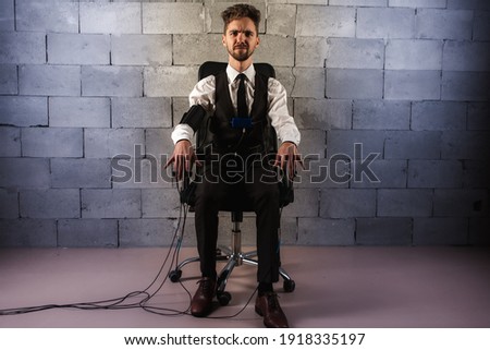 frightened, worried, pensive, man sitting on a chair, testing on a polygraph, wearing sensors to pass a polygraph, sitting on a background of gray brickwork, looking straight