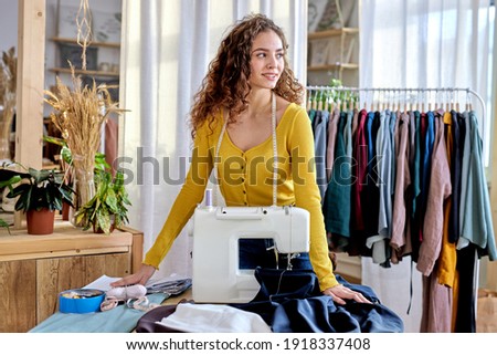 tailor making a garment in her workplace, stand in contemplation looking at side, have rest. hobby sewing as a small business concept. in bright modern room. fashion, style concept