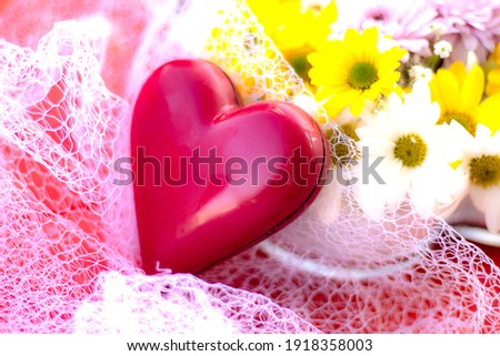 
Heart-shaped red chocolate stands on white tulle. there are daisies next to you. concept about valentines day. 