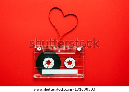 Vintage audio cassette with loose tape shaping a heart on red background 
